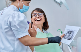 Woman smiling with dentist while reviewing X-ray