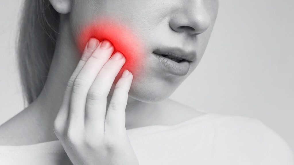 Grayscale nose-to-neck image of woman pressing hand to sore cheek highlighted red